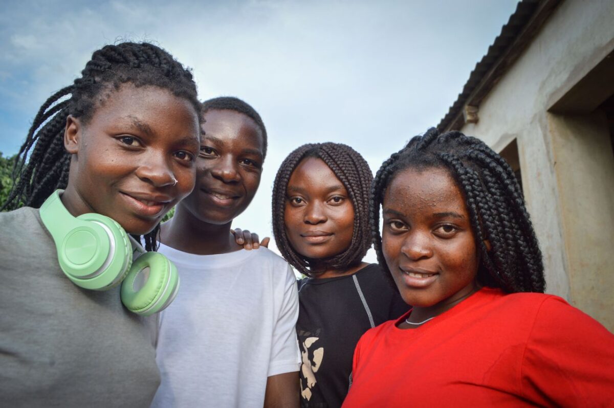 A group of friends with braids smiling outdoors in Molumbo, Mozambique, showcasing friendship and joy.