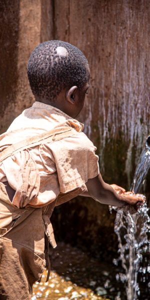 A child gathers clean water from an outdoor tap, highlighting access to essential resources.